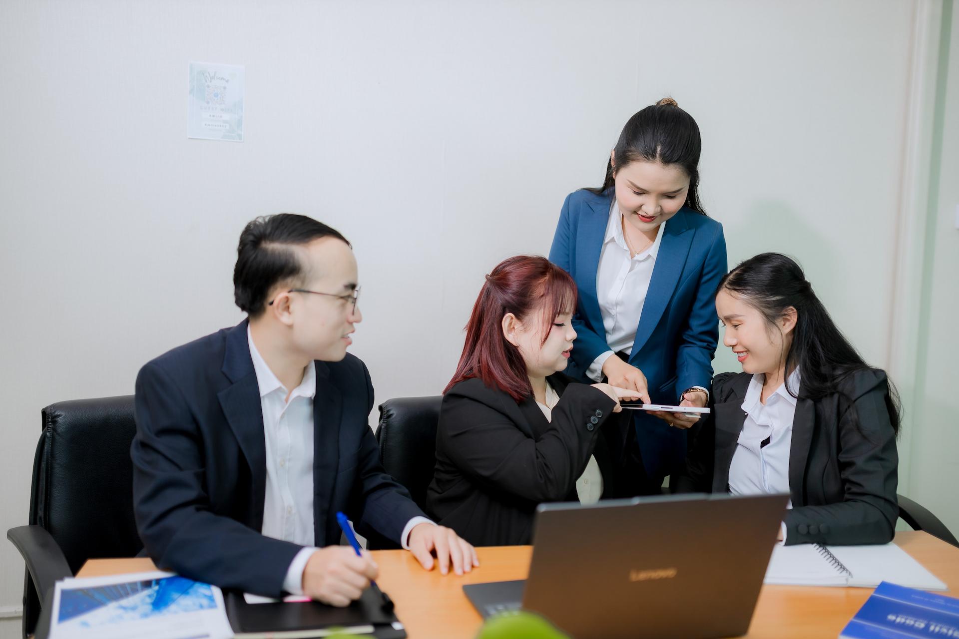 A diverse group of four people in business attire are gathered around a table in an office setting.