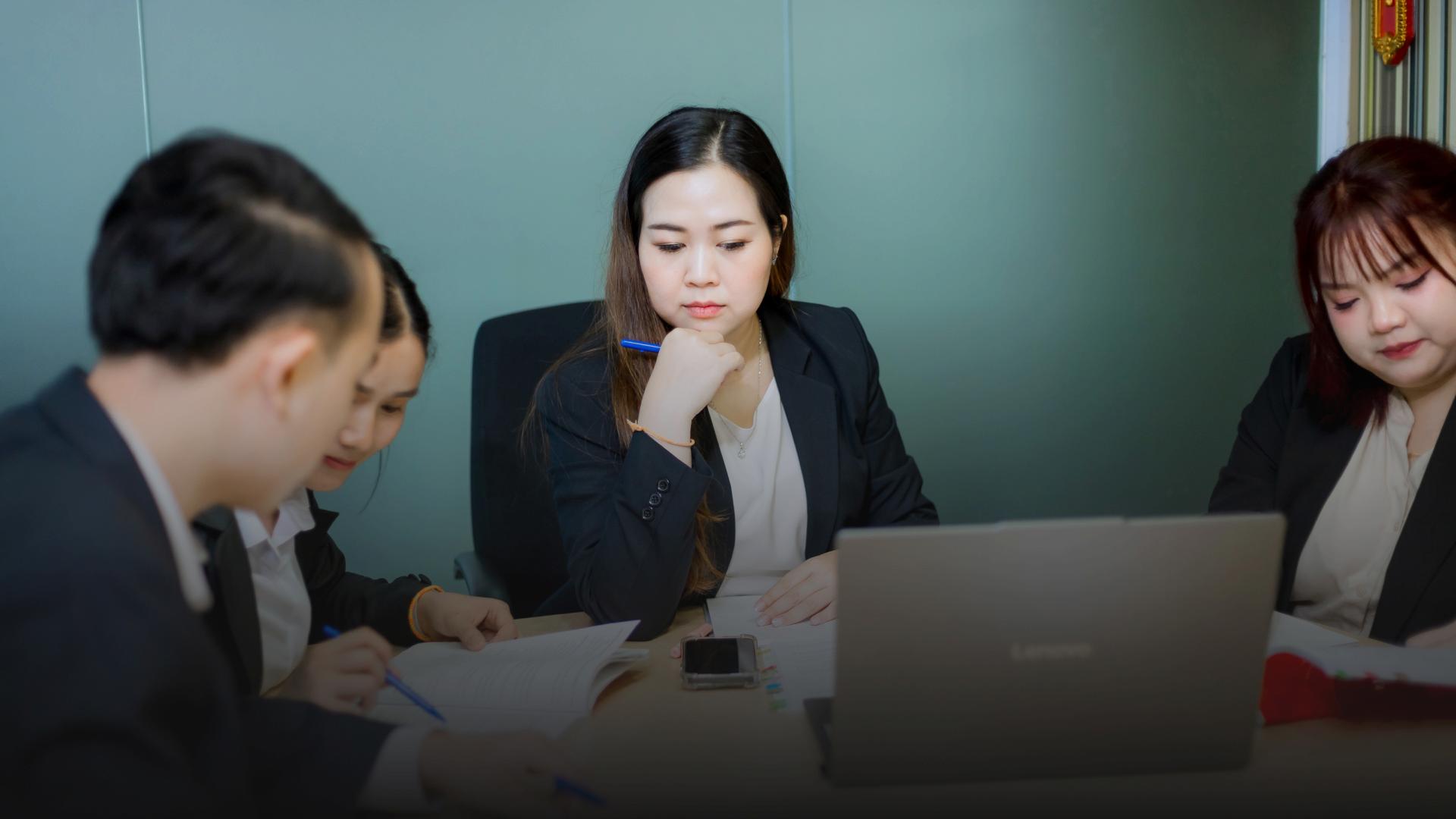 A group of people in business attire are gathered around a table, appearing to be in a meeting.