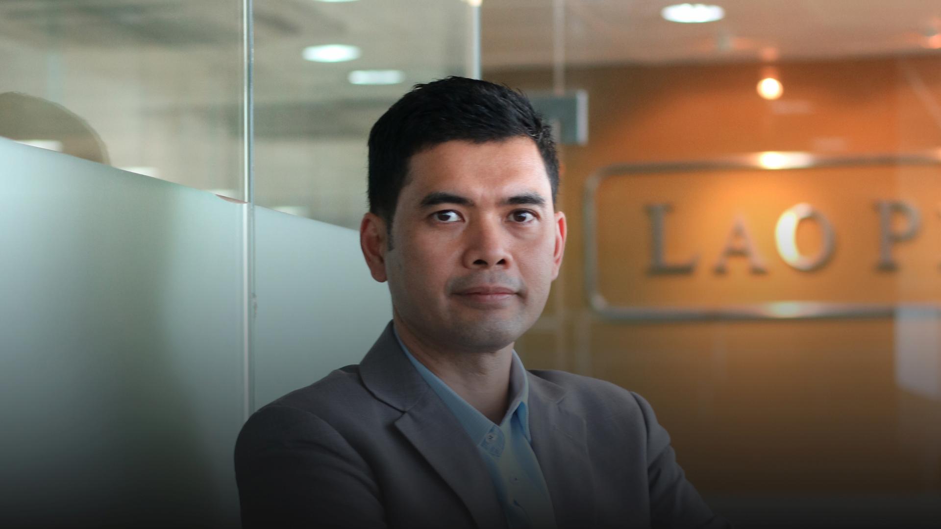 A man in a suit and blue shirt looks directly at the camera.