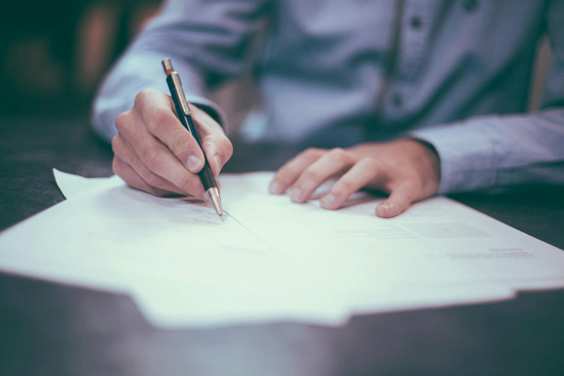 A person is writing on a piece of paper with a pen.